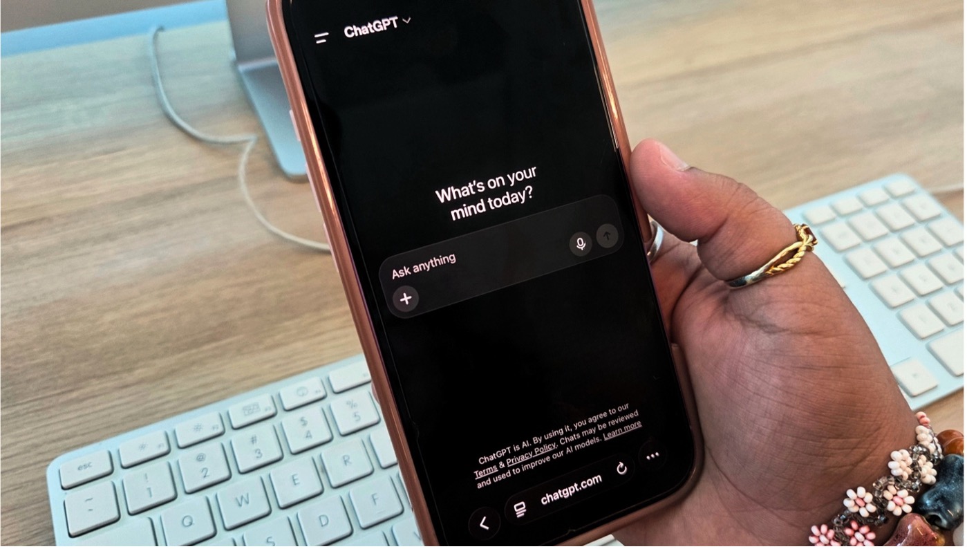 Student holds a smartphone displaying ChatGPT over a computer keyboard