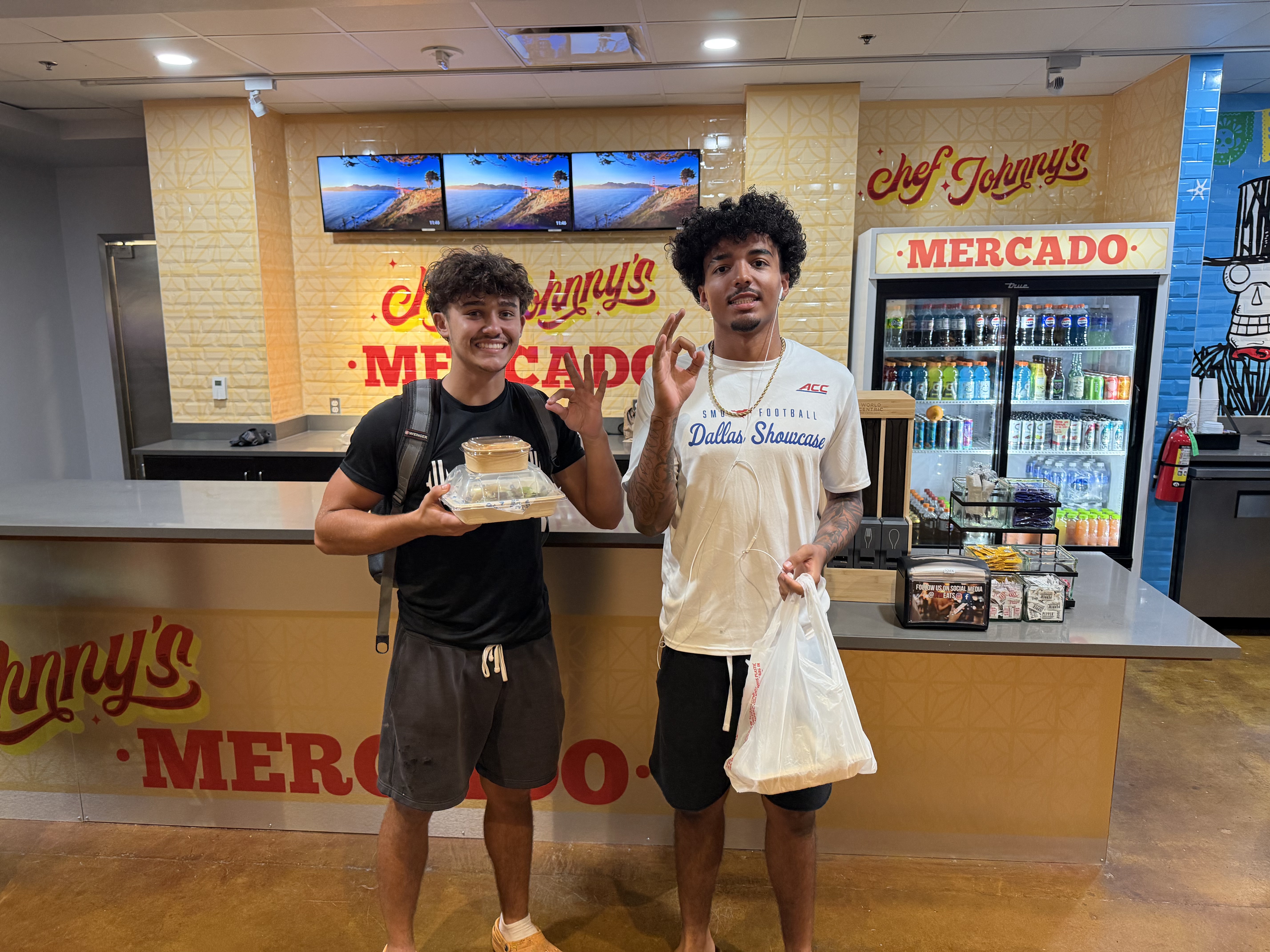 Two UIW students holding food in front of Chef Johnny’s Mercado at the new La Gloria campus location.